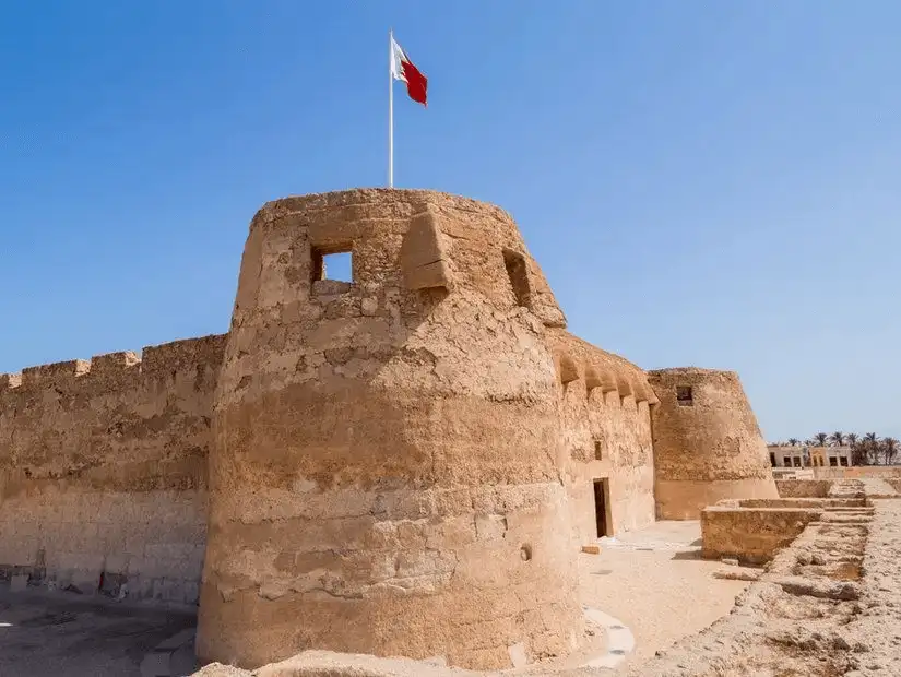 The historic Bahrain Fort, a UNESCO World Heritage site, standing strong with its ancient limestone walls under the Bahraini flag.