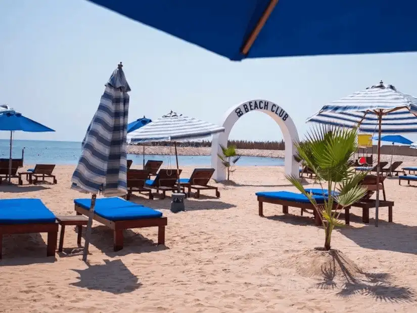 Beach club area with blue sun loungers and striped umbrellas.