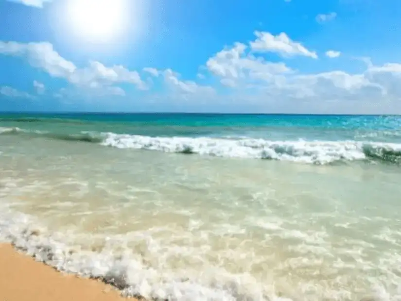 A bright, sunny day at a sandy beach with turquoise waves gently rolling onto the shore.