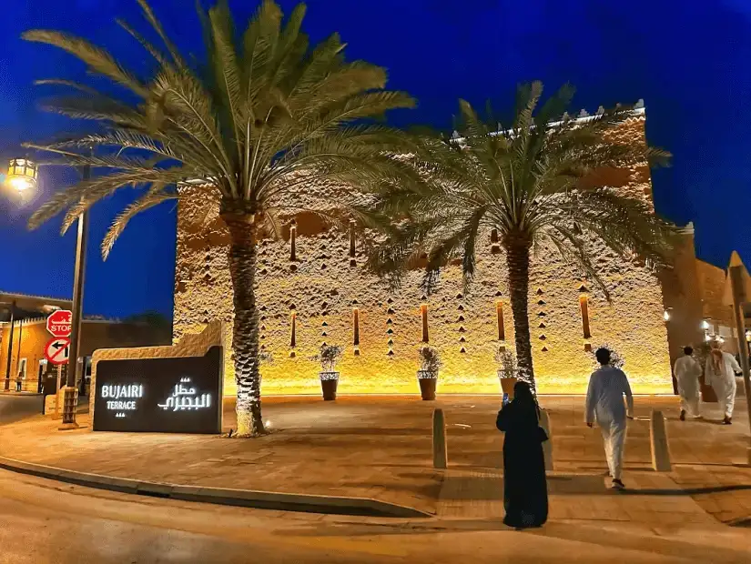 A beautifully lit evening scene at the Bujairi Terrace, capturing its luxurious architecture and palm-lined streets as the night sky sets in.