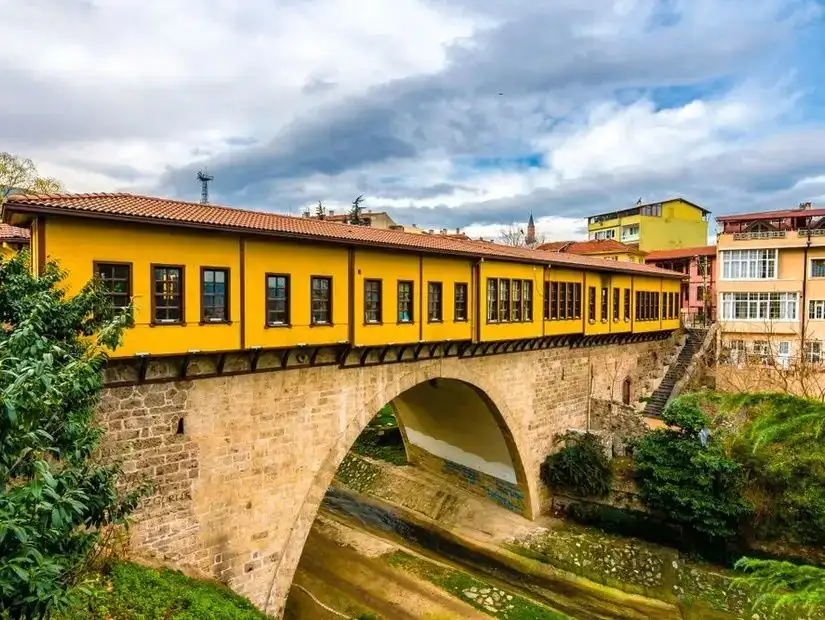 The famous covered bridge in Bursa with vibrant yellow walls, arching over a river surrounded by traditional buildings.