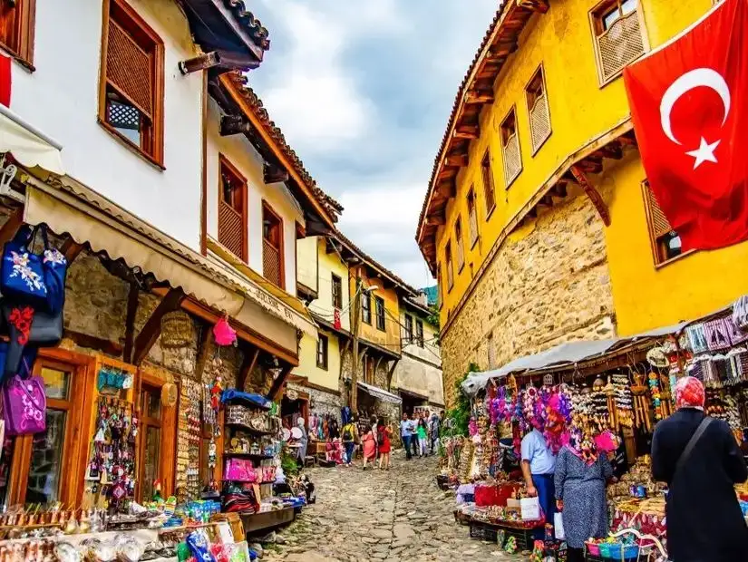 A cobbled street in Bursa, lined with vibrant yellow and white buildings, with a Turkish flag hanging from one of the houses.