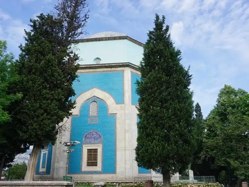 The beautiful Green Mosque in Bursa, surrounded by palm trees, with its intricate turquoise minaret and a calm garden.