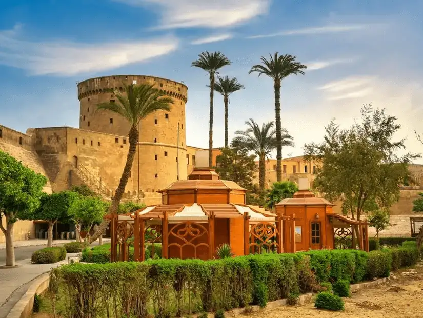 A scenic view of the historic Cairo Citadel, surrounded by lush gardens and palm trees.