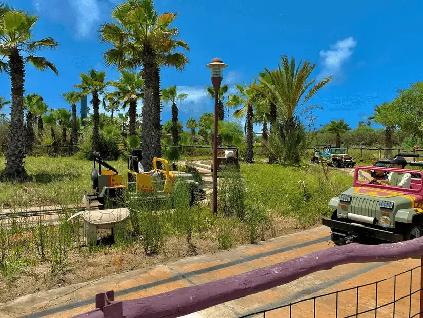 Children's amusement park with miniature jeeps among palm trees.