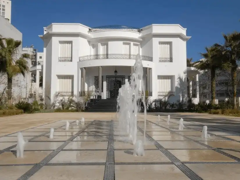 Elegant white mansion with a fountain in the front courtyard.