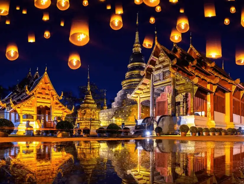 Lanterns float above a beautifully lit temple in Chiang Mai at night.