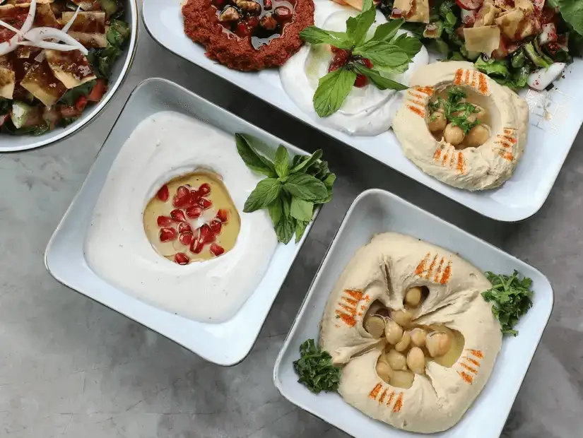 A selection of Middle Eastern dips including hummus and baba ganoush, garnished with fresh herbs and pomegranate seeds.