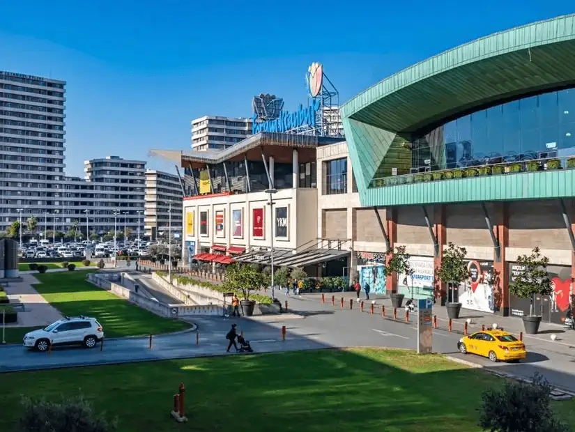 Shoppers enjoy a sunny day outside a contemporary mall with a sprawling plaza.