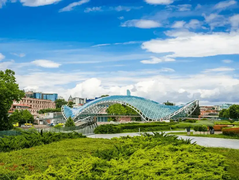 The iconic glass bridge in Tbilisi, Georgia, surrounded by lush greenery and city views.