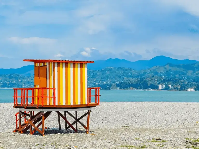 A vibrant beach scene with crystal-clear waters and lush green mountains in the background.