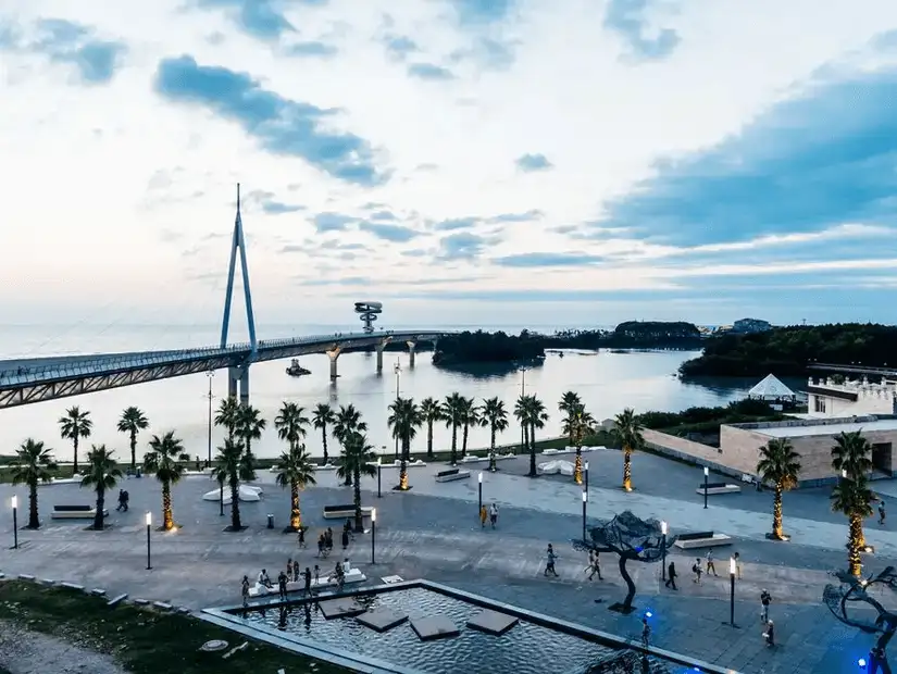 A picturesque riverside park with palm-lined paths and a modern bridge at sunset.