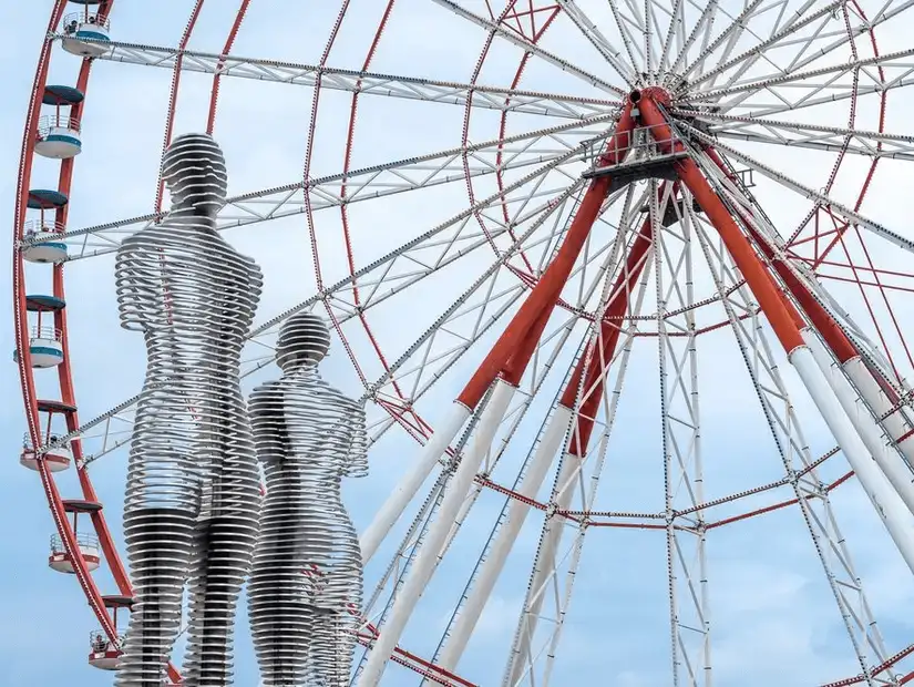 Two iconic metal sculptures with a ferris wheel in the background, symbolizing love and connection.