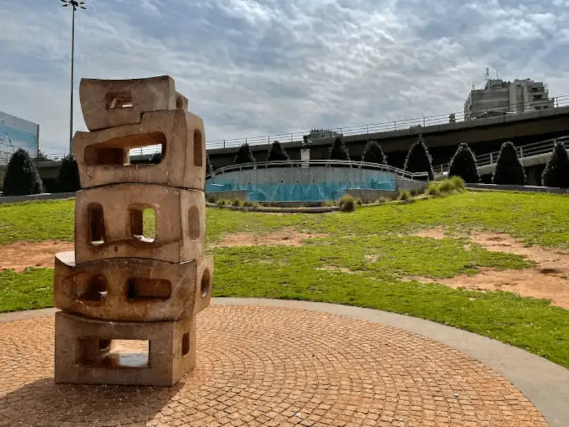 A stone sculpture in a park with green grass and a fountain in the background.