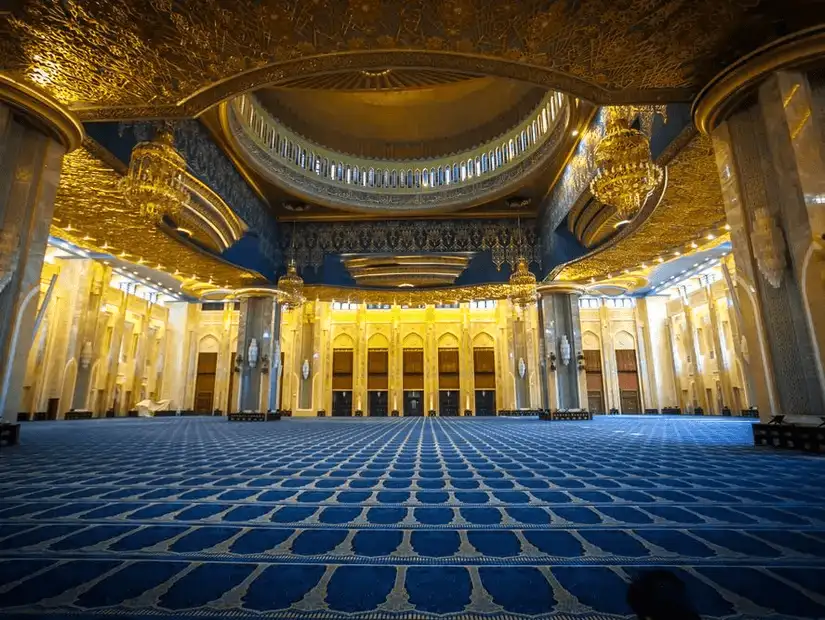 The opulent interior of the Grand Mosque in Kuwait, featuring golden decor and intricate architecture.