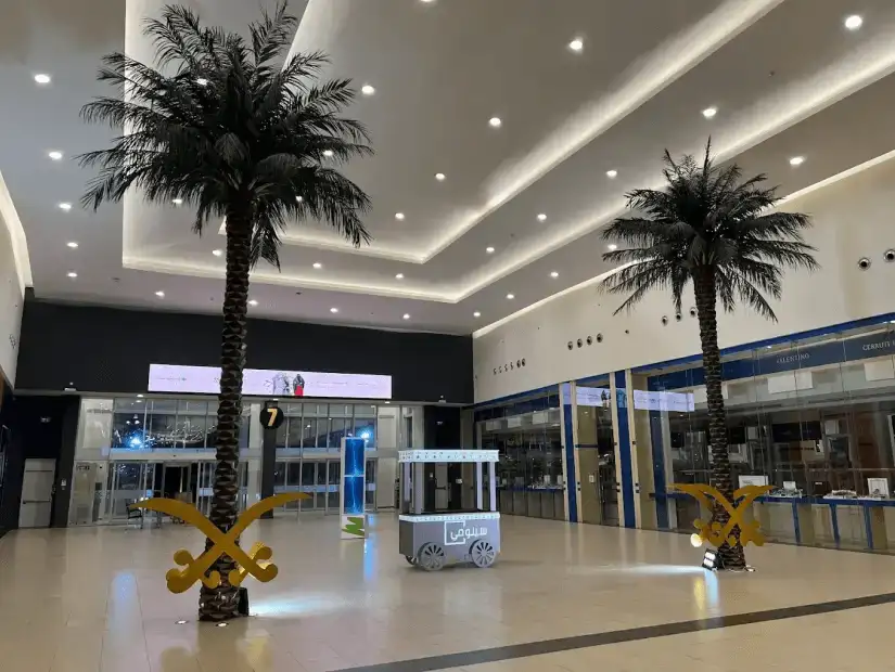 A spacious mall entrance with decorative palm trees and a bright, clean design, welcoming shoppers into the space.
