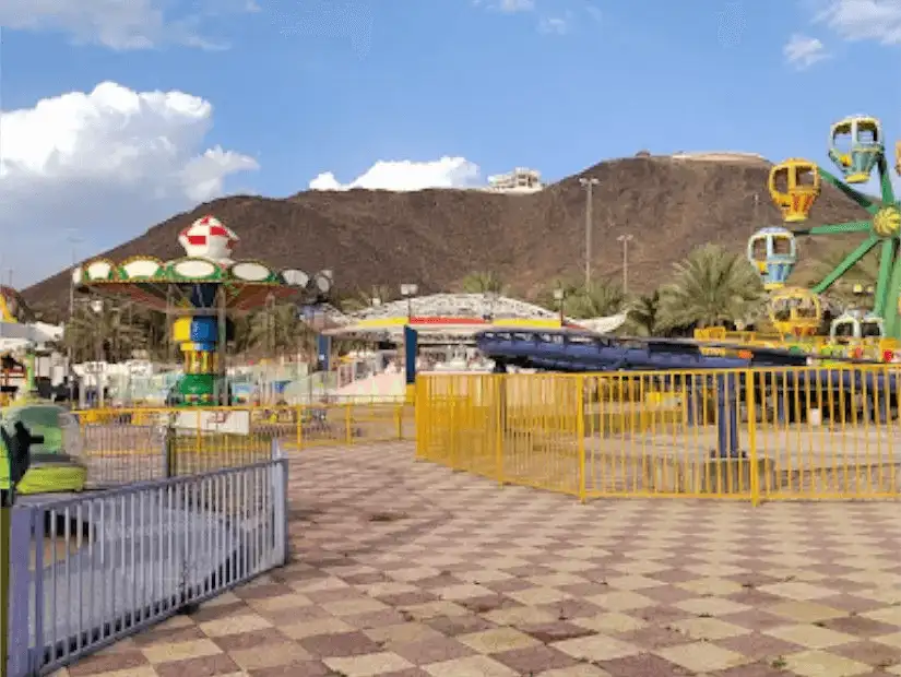 A lively amusement park with colorful rides set against the backdrop of a rocky hill.