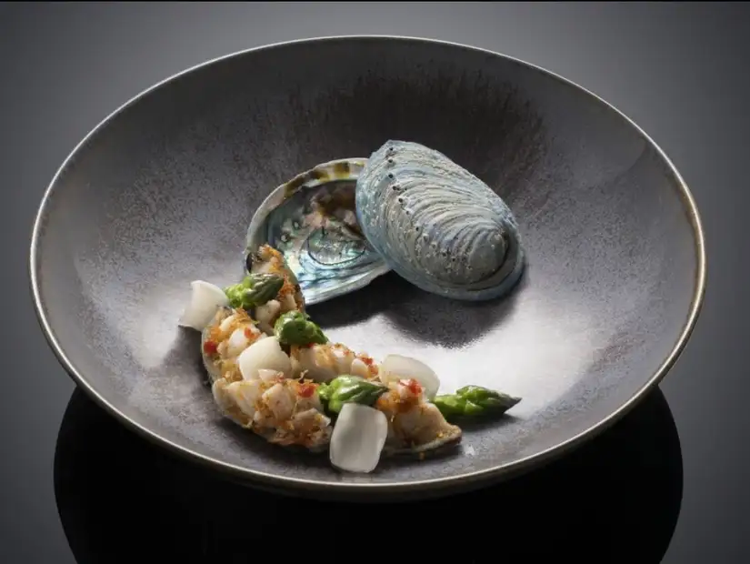 A delicate seafood dish featuring succulent shellfish accented with vibrant green asparagus and a decorative shell.
