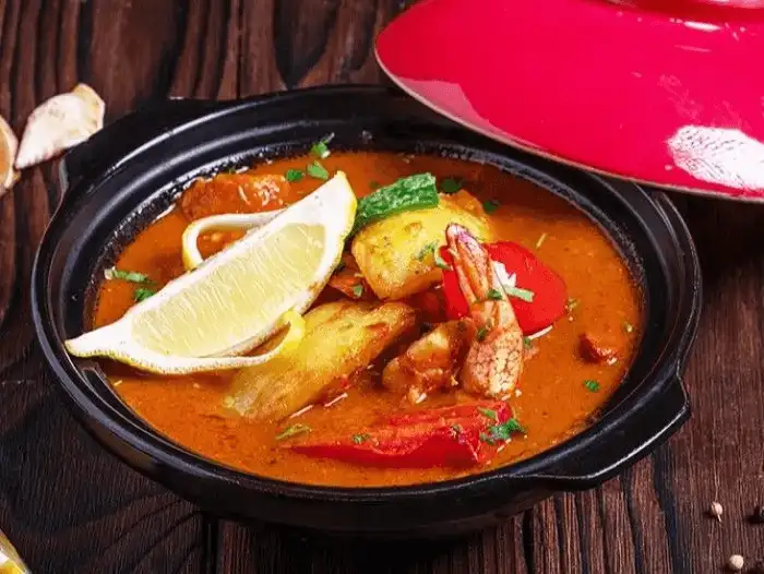 Hearty seafood stew in a traditional pot, garnished with a wedge of lemon.