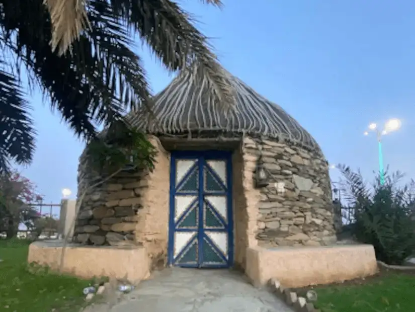 A quaint stone hut with a thatched roof, nestled in a lush park setting.