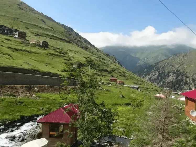 A tranquil view of the Hıdırnebi highlands, with rolling green hills and cozy mountain cabins.