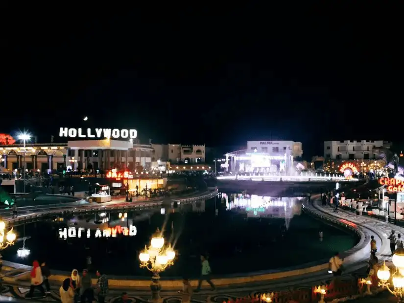 A vibrant night scene at a themed entertainment center styled like Hollywood, glowing with lights and bustling with activity.