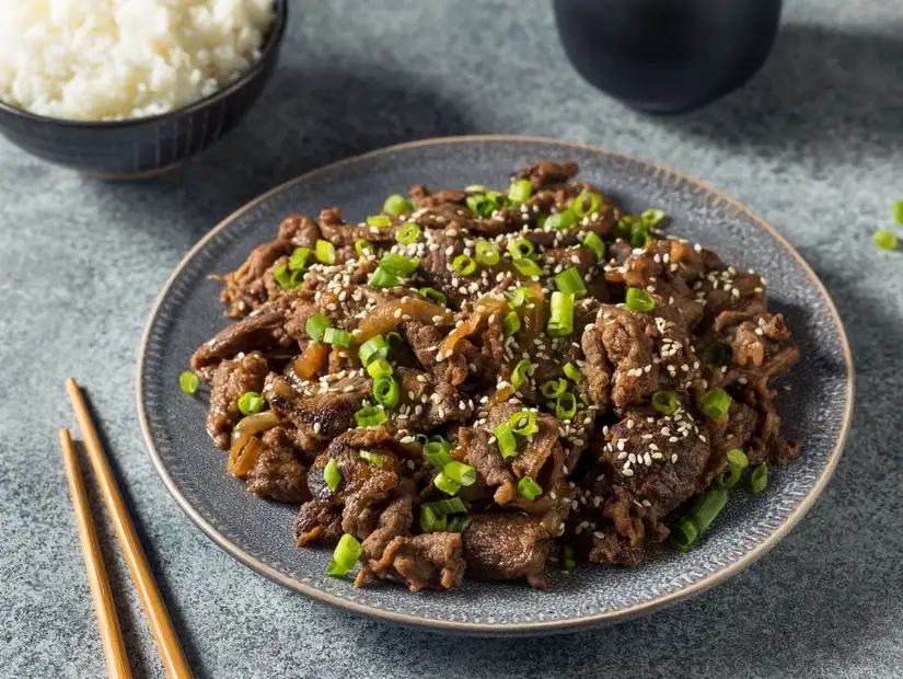 Savory beef bulgogi with scallions and sesame seeds, served beside steamed rice.