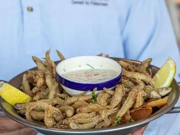 A plate of crispy fried small fish, presented by the chef in a casual dining setting.