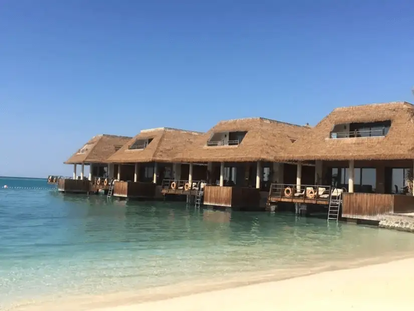 Overwater bungalows with thatched roofs nestled along a crystal-clear shoreline, perfect for a serene getaway.