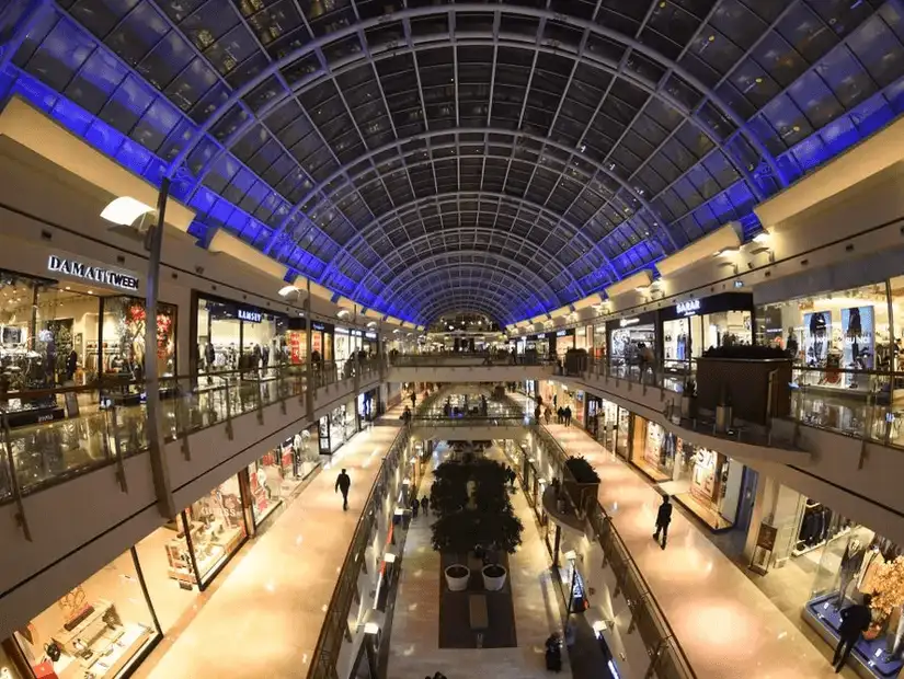 Inside a grand shopping atrium, shoppers experience luxury beneath a vast glass ceiling.