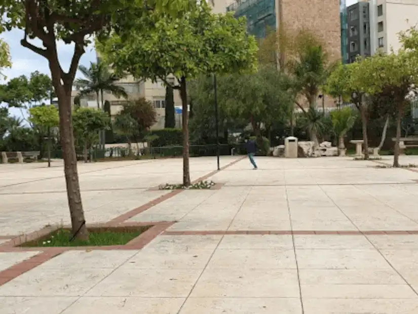 An empty plaza with trees and surrounding buildings in the background.