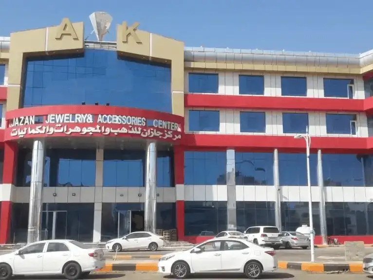 A large shopping center with a bold red and white exterior in Jizan.