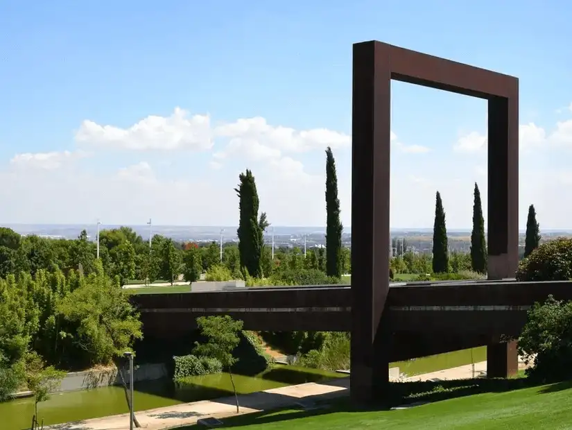 A vast green park featuring modern art, wide walkways, and tranquil water views.