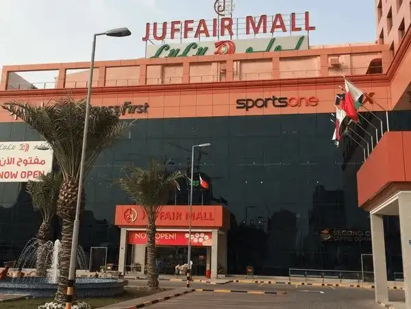 The vibrant exterior of Juffair Mall, with clear signage and palm trees at the front.