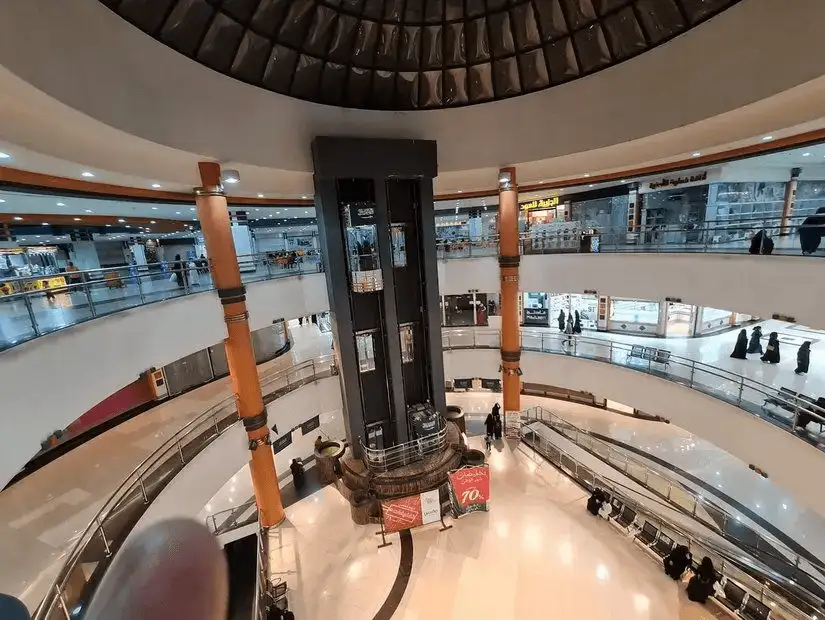 Interior of a modern shopping mall with multiple floors and a central elevator.