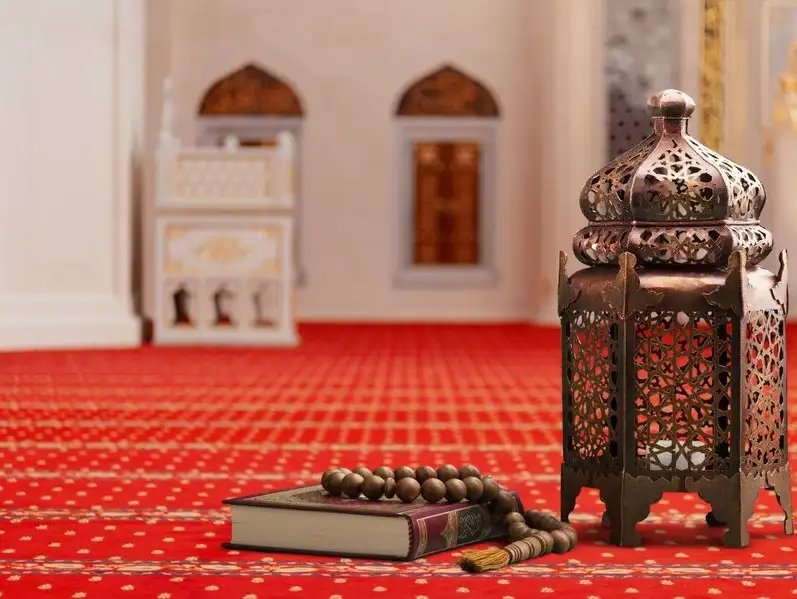 A decorative lantern and a Quran on a red carpet inside a mosque.