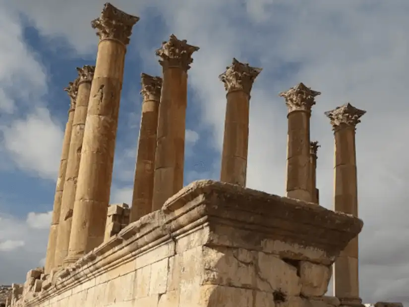 Ancient stone columns standing tall against a backdrop of blue sky and clouds.