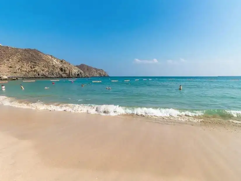 A scenic view of the beach in Khorfakkan, with blue umbrellas and a calm, clear sea stretching into the horizon.