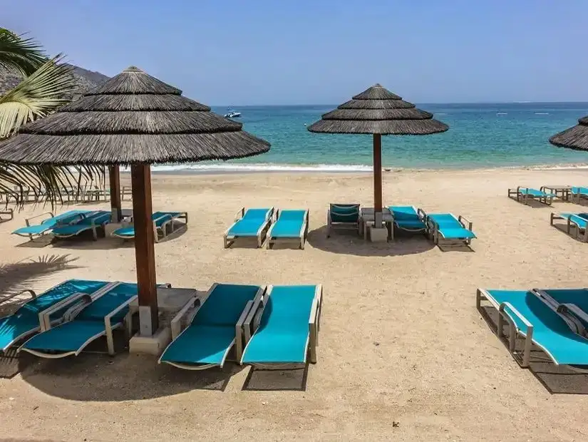 A tranquil beach view in Khorfakkan with umbrellas and lounge chairs facing the blue sea under the bright sky.