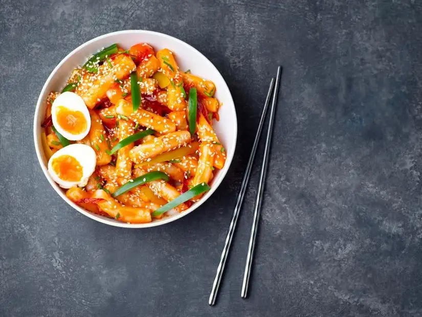 Spicy Korean rice cakes with boiled eggs and vegetables, garnished with sesame seeds.