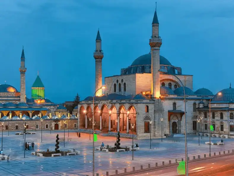 The illuminated Mevlana Museum and its surrounding courtyard at dusk in Konya.