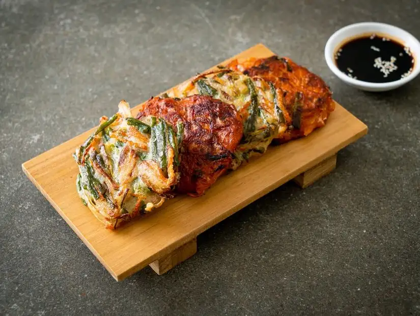 Korean seafood pancake with green onions, served on a wooden board with dipping sauce.