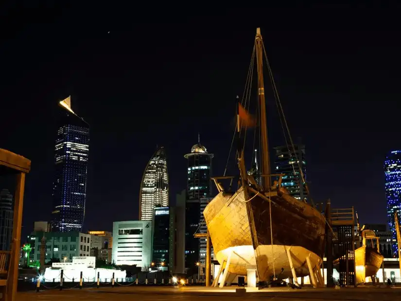 The traditional dhow displayed outside the Kuwait National Museum, with the modern city skyline in the background.