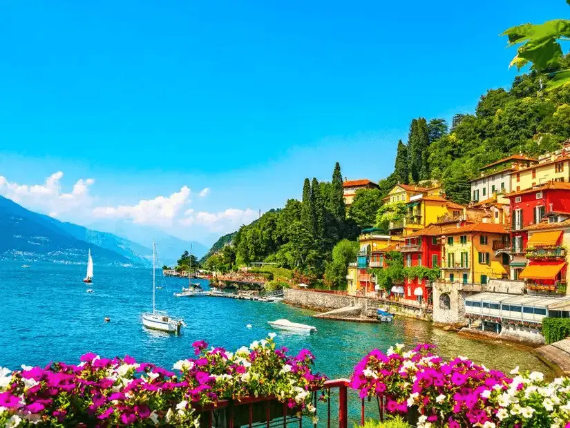 Serene waters of Lake Como with a foreground of vibrant flowers, showcasing the peaceful and picturesque lakeside lifestyle.