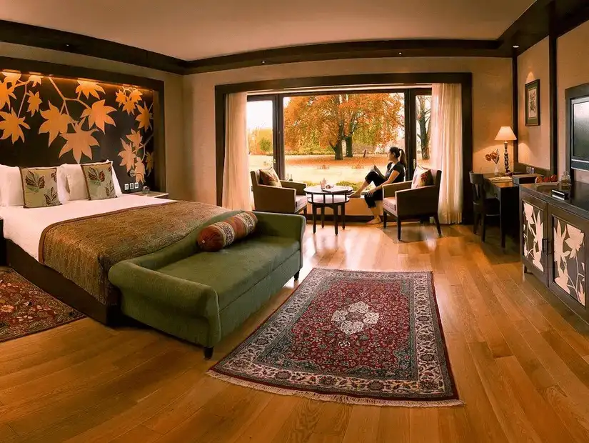 A cozy hotel room with a scenic view of autumn foliage through large windows.