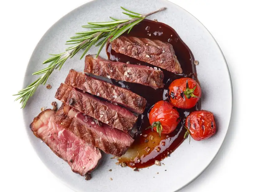 Elegantly plated steak slices with roasted tomatoes and fresh rosemary on a sleek gray plate.