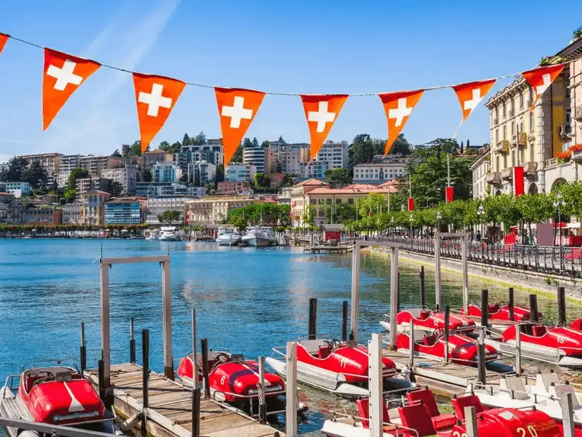 Vibrant waterfront in Lugano decorated with Swiss flags.