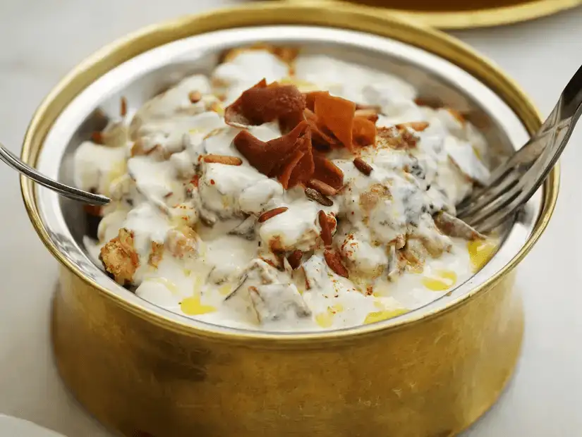 A traditional dish served in a brass bowl with yogurt and crispy bread.