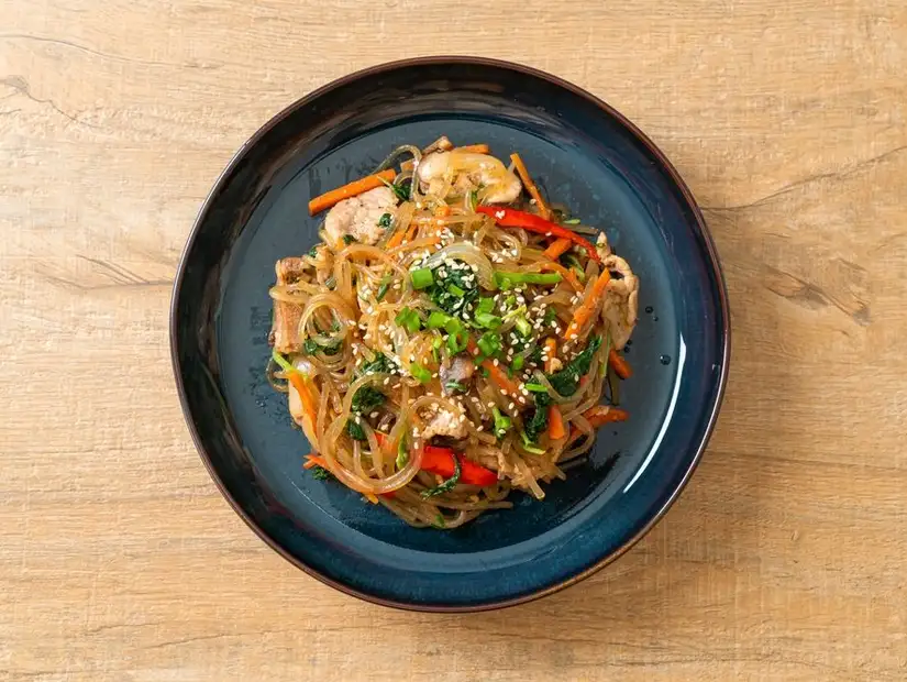 Stir-fried Korean glass noodles with vegetables and strips of meat, topped with sesame seeds.