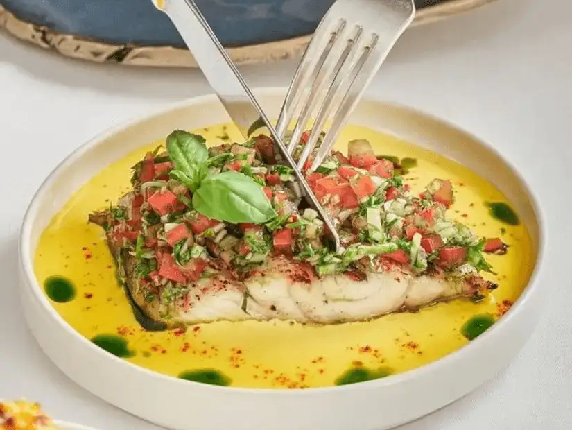 A beautifully plated fish fillet topped with fresh tomato and herb salsa, served in a vibrant yellow sauce.